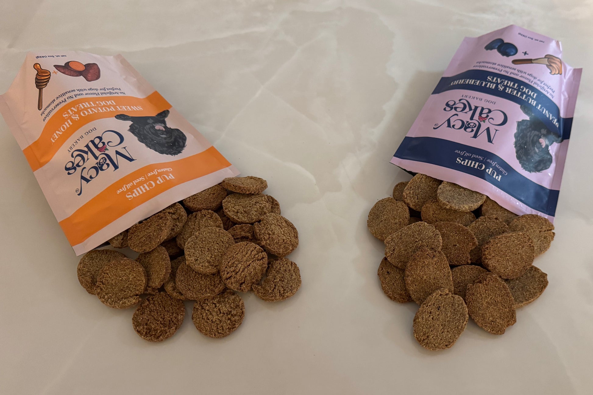 Two bags of Macy Cakes dog treats with open packaging on a white counter